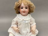 une image représentant une poupée en porcelaine assise par terre, vêtue d'une robe blanche et de chaussures marron