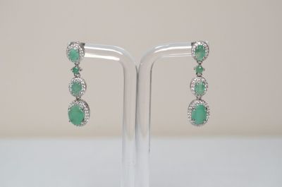 a pair of emerald and diamond earrings on a stand