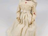 une image représentant une poupée en forme de religieuse, vêtue d'une robe blanche ornée d'une croix rouge