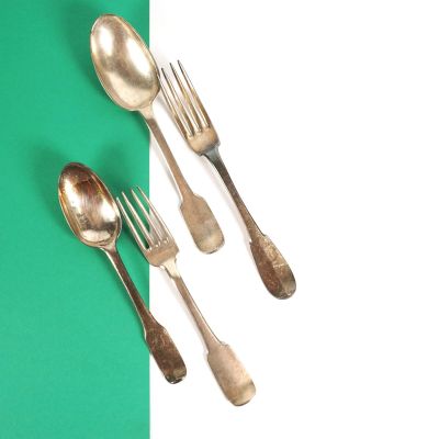 trois cuillères en argent et deux fourchettes en argent sur un fond vert et blanc