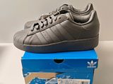 Des chaussures adidas Superstar grises et noires posées sur une boîte bleue