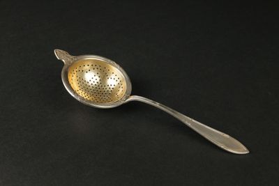 une cuillère en argent surmontée d'une passoire en métal