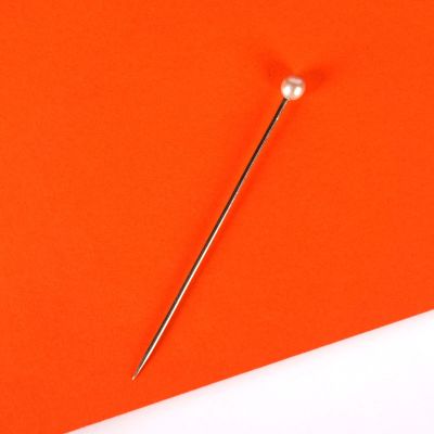 une aiguille est posée sur un morceau de papier orange