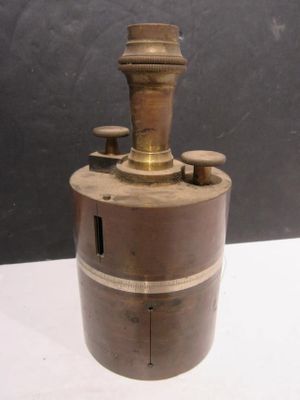 un cylindre ancien plaqué laiton, muni de quatre boutons, posé sur une table blanche