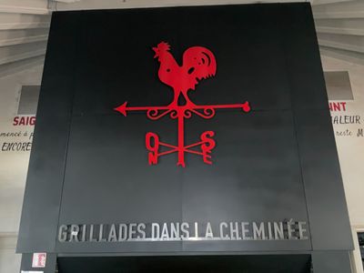 une enseigne noire et rouge sur laquelle figure un coq rouge