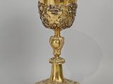 une coupe en or richement décorée, posée sur un socle, sur fond blanc