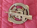 une broche en métal représentant un pistolet, posée sur une couette rose