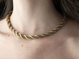 La femme porte une robe noire et un collier en or.