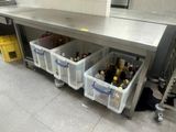 Les bouteilles de vin sont rangées dans des bacs en plastique sous un comptoir en acier inoxydable.