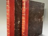 an old book with red bindings sitting on top of a table