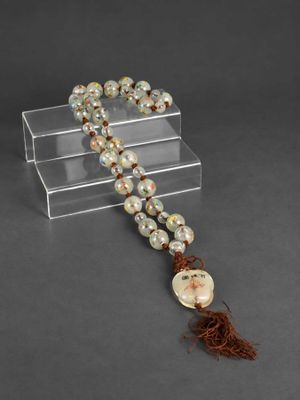 un chapelet orné de perles et d'un pompon, monté sur un support transparent