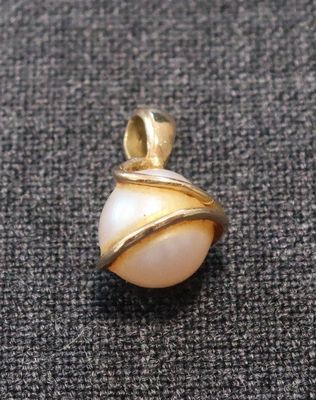 un gros plan d'un pendentif en perle blanche et or posé sur un tissu noir