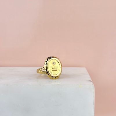 une bague en or surmontée d'une pièce de monnaie posée sur un bloc de marbre