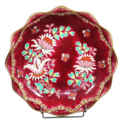 une assiette rouge décorée de fleurs, posée sur un socle