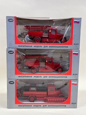 trois camions de pompiers rouges dans des boîtes, posés sur une surface blanche