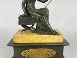 une statue antique en bronze représentant une femme assise sur une boîte