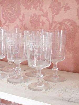 plusieurs verres à vin vides posés sur une étagère devant un mur recouvert de papier peint