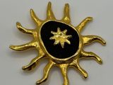a close up of a gold sun brooch with a black center