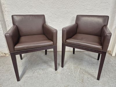 une paire de fauteuils en cuir marron posés sur un sol en béton, près d'un mur blanc