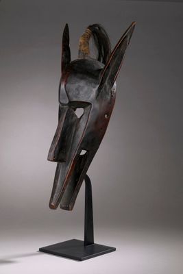 une image représentant un masque en bois posé sur un socle noir