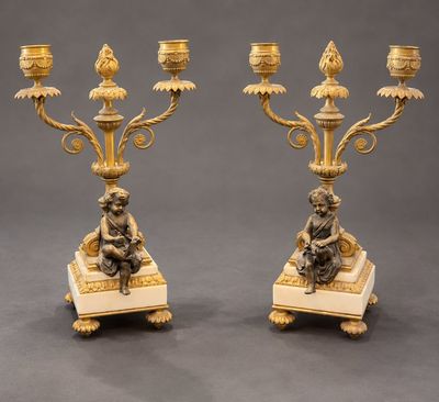 paire de chandeliers anciens en laiton ornés de figurines sur des socles en marbre