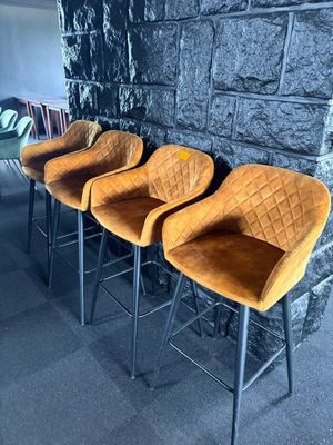 Quatre tabourets de bar en velours orange sont alignés contre un mur en pierre