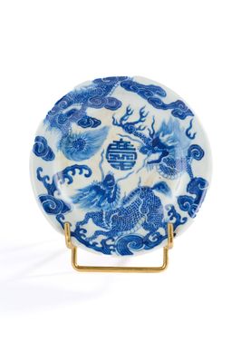 assiette bleue et blanche ornée d'un dragon, posée sur un socle doré
