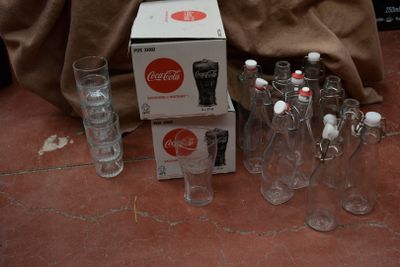 Des bouteilles et des verres sont posés par terre à côté d'une caisse de Coca-Cola.