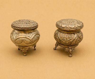 paire de petits pots anciens en métal argenté sur un socle, sur fond marron