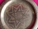 a silver plate with a design on it on a pink surface