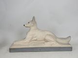 statue of a dog laying down on a base on a white background