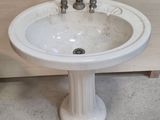 a white pedestal sink with two faucets on it