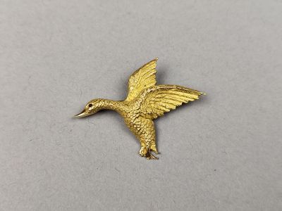 un gros plan d'une broche en forme de colibri doré posée sur une surface blanche