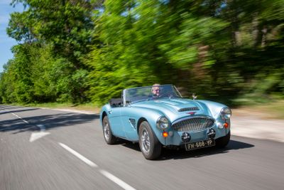 a blue car driving down the road with trees in the background