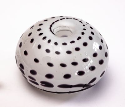 un vase blanc parsemé de taches noires, à côté d'un petit objet blanc