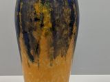 a blue and yellow vase sitting on a glass stand