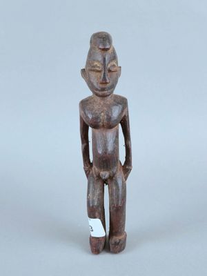 une vieille statue en bois représentant un homme debout, les mains dans les poches