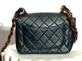 a small black purse sitting on top of a white pedestal