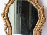 un miroir doré accroché au mur, à côté d'un mur blanc