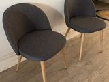 pair of grey chairs with wooden legs in front of a white wall