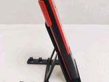 a red and black cellphone on a stand on a white surface