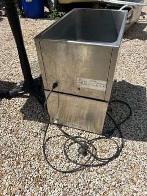 une image représentant un évier en métal posé sur un sol recouvert de gravier