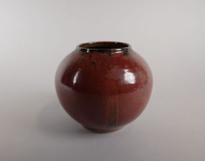 un vase marron posé sur une table, avec un mur blanc en arrière-plan