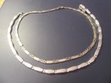 two silver necklaces on display on a table with a black background