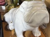 une statue de chien blanc posée sur une étagère, à côté d'une boîte d'assiettes