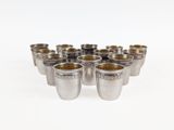 six silver shot glasses lined up in a circle on a white surface