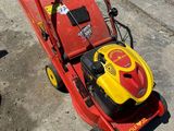 une tondeuse à gazon rouge et jaune posée sur le trottoir