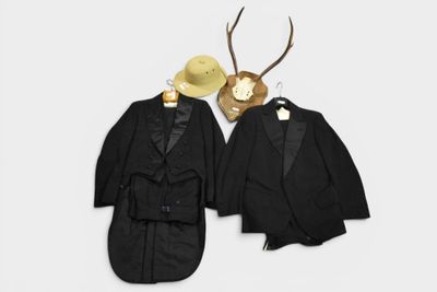 two suits and a hat are hanging on a wall