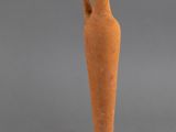 un petit vase muni d'une anse, posé sur un socle à côté de quelques figurines