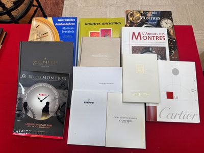 de nombreux livres posés sur une table rouge, avec une horloge en arrière-plan